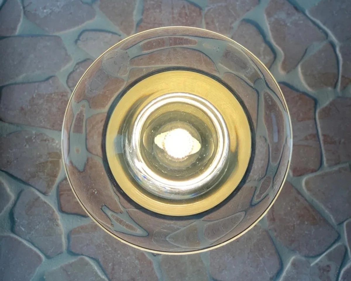Looking down into a transparent glass of white wine on a stone-tiled surface.