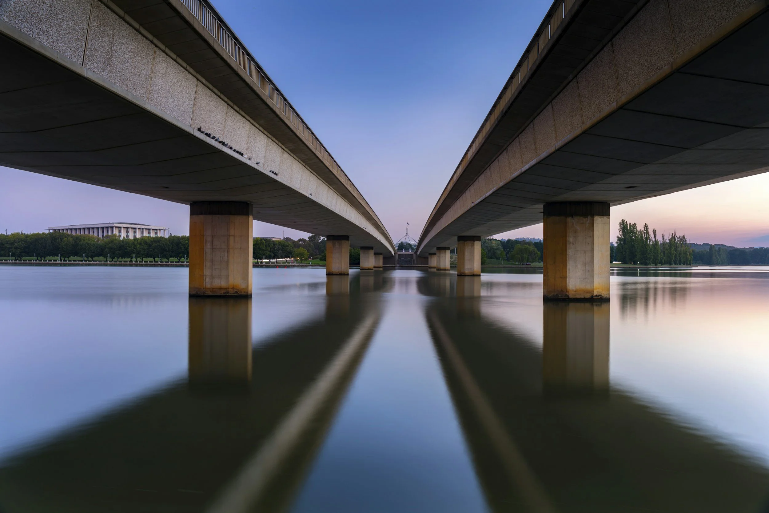 Two bridges over a calm river at sunset, with reflections in the water.