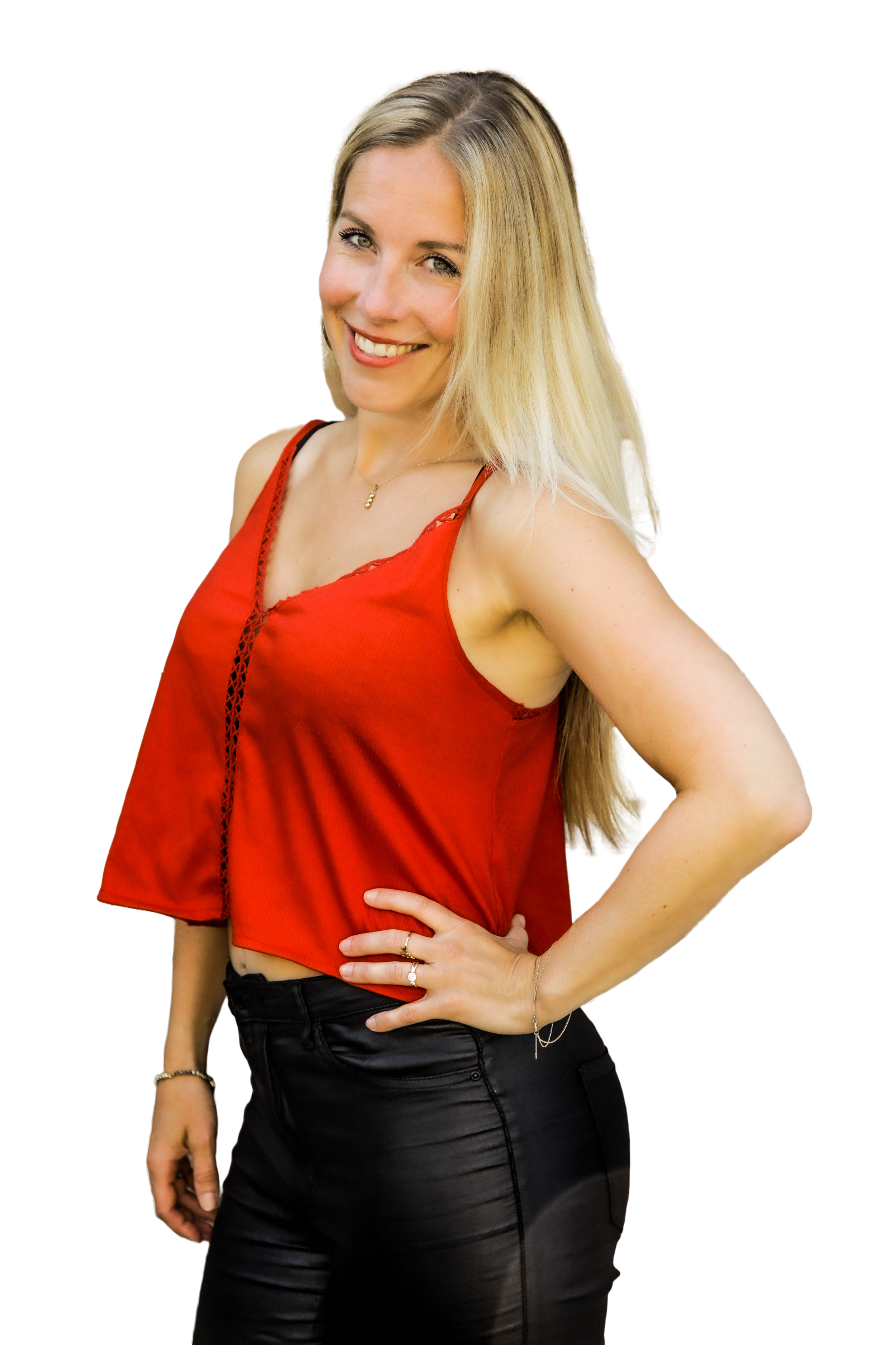 A woman with long blonde hair smiling, wearing a red sleeveless top and black pants, standing with one hand on her hip.
