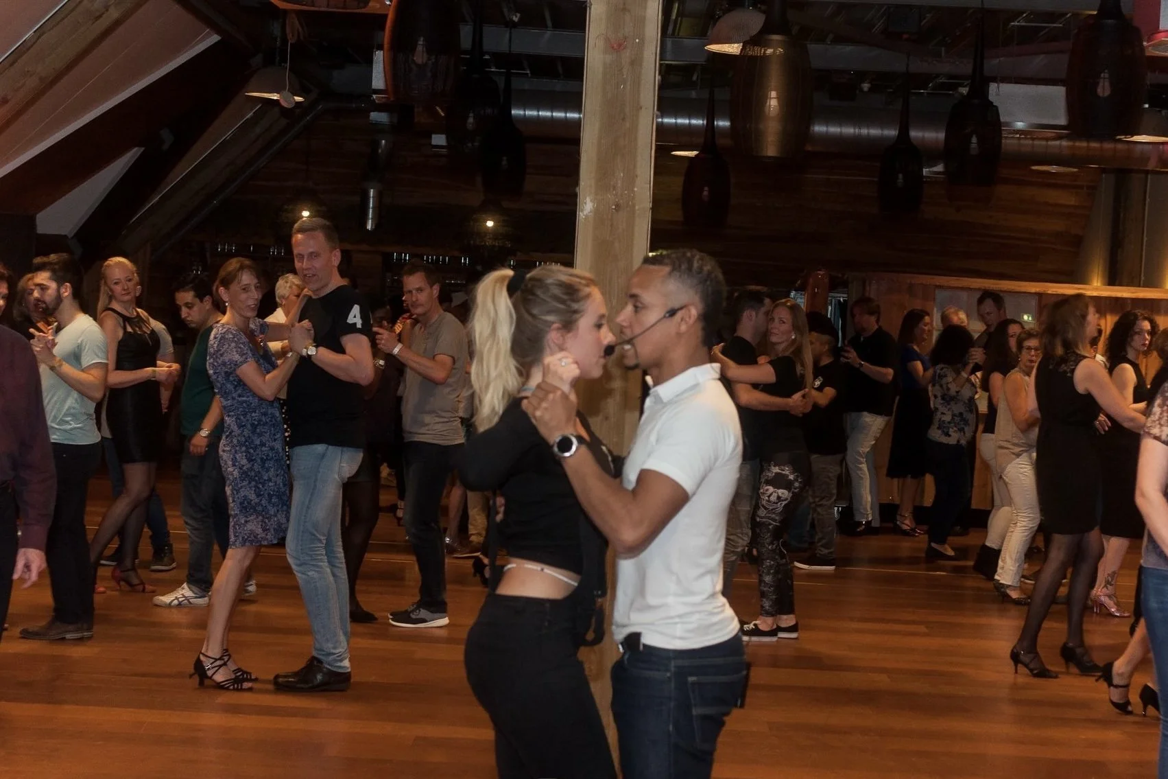 Couple dancing closely in the foreground at a crowded dance event with many other couples dancing in the background.