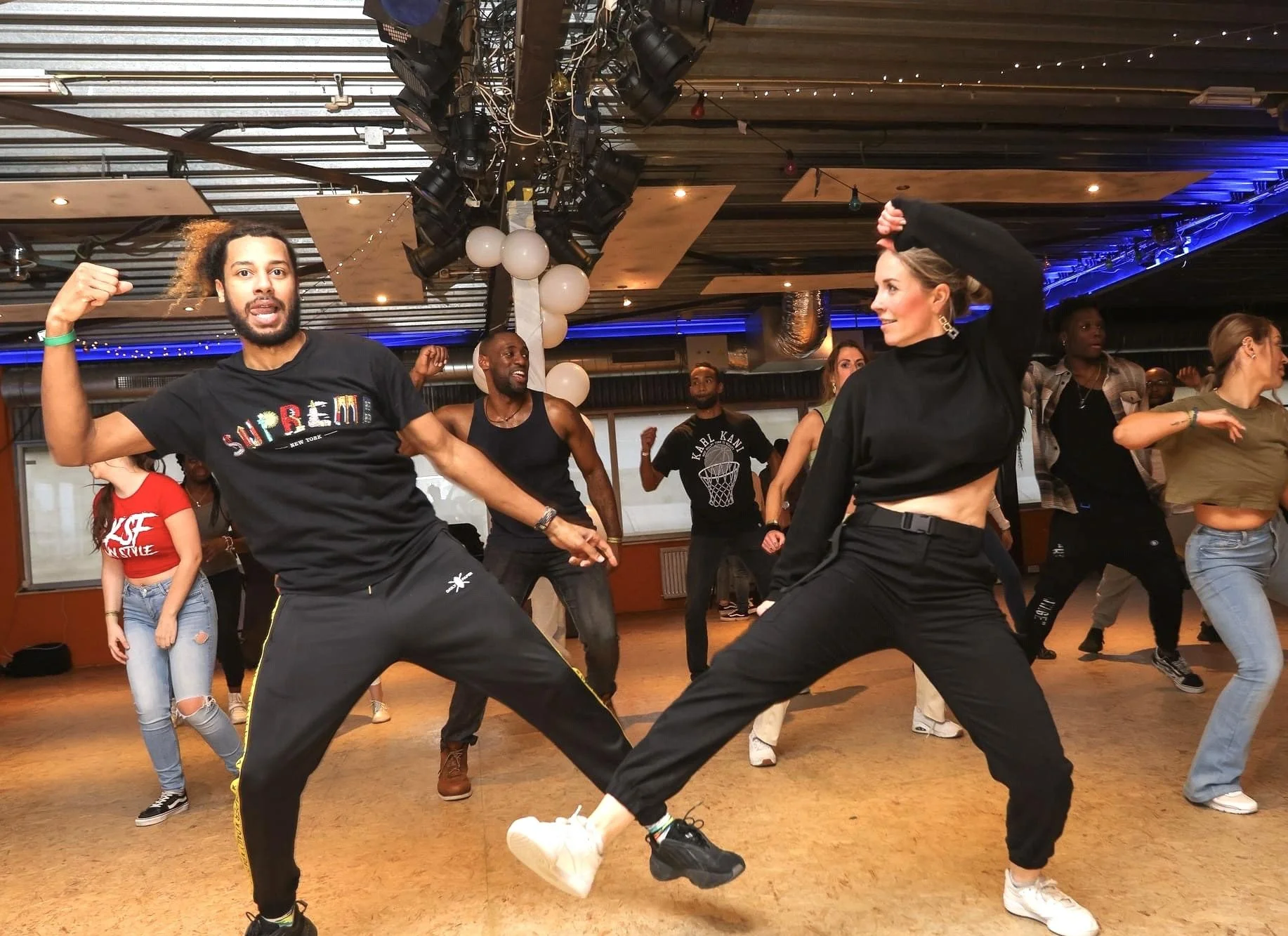 Group of diverse people dancing together in a studio or dance class, with some in energetic poses and expressions.