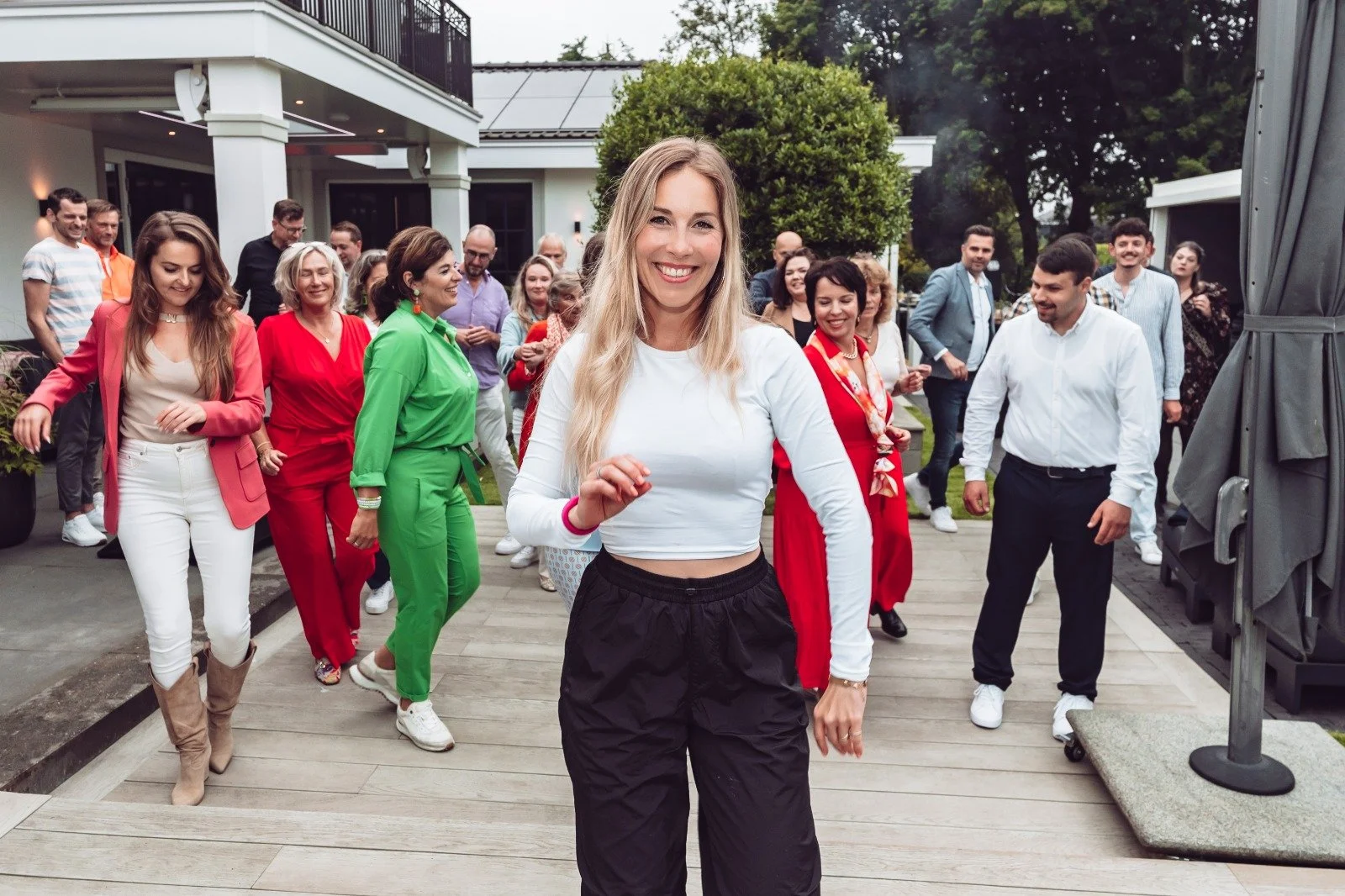 People dancing and enjoying a celebration on a patio outside a house, with a smiling woman in the foreground and a group of people behind her.