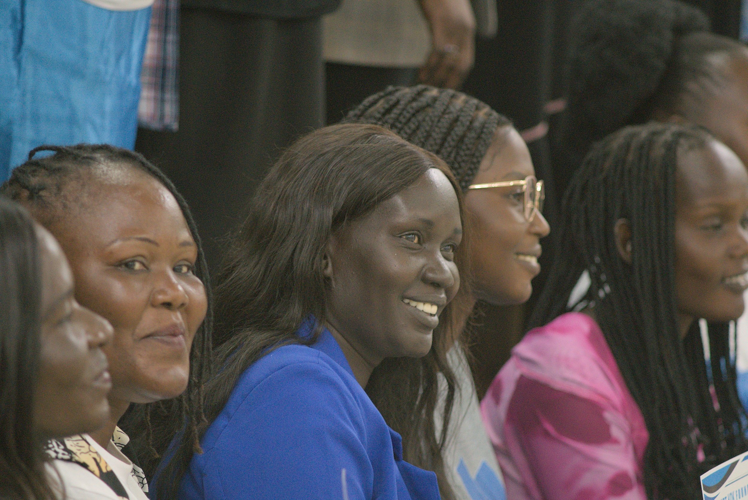 Group of women sitting side by side at an event, smiling and looking forward.