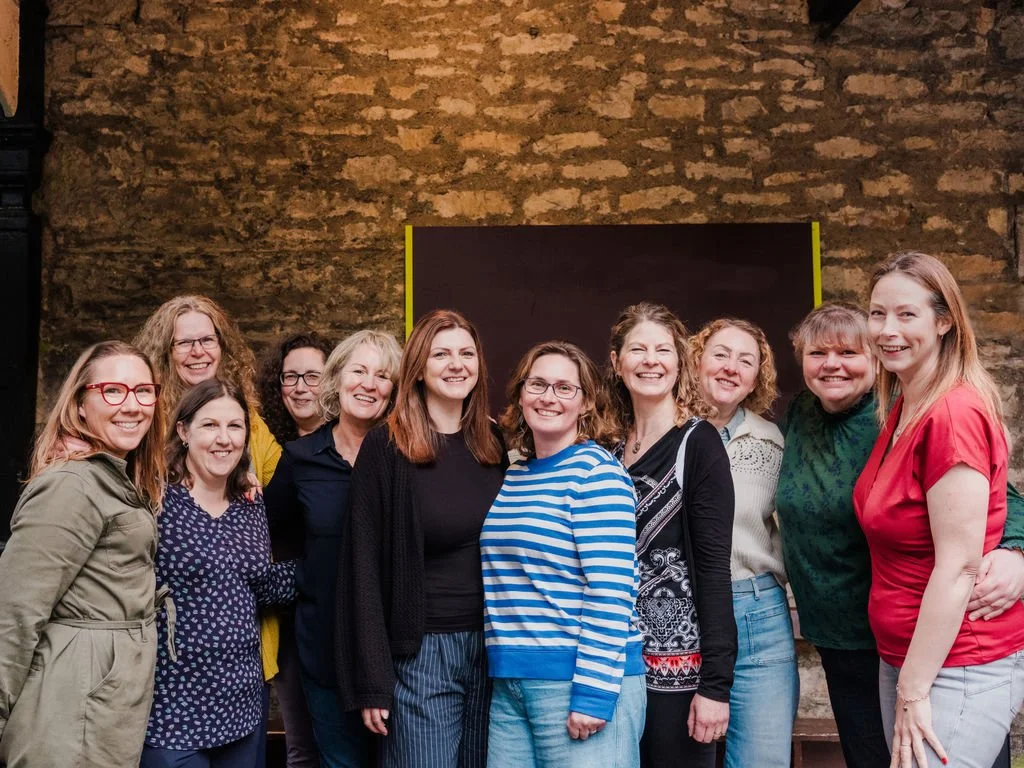 Group of ten smiling women standing in front of a brick wall