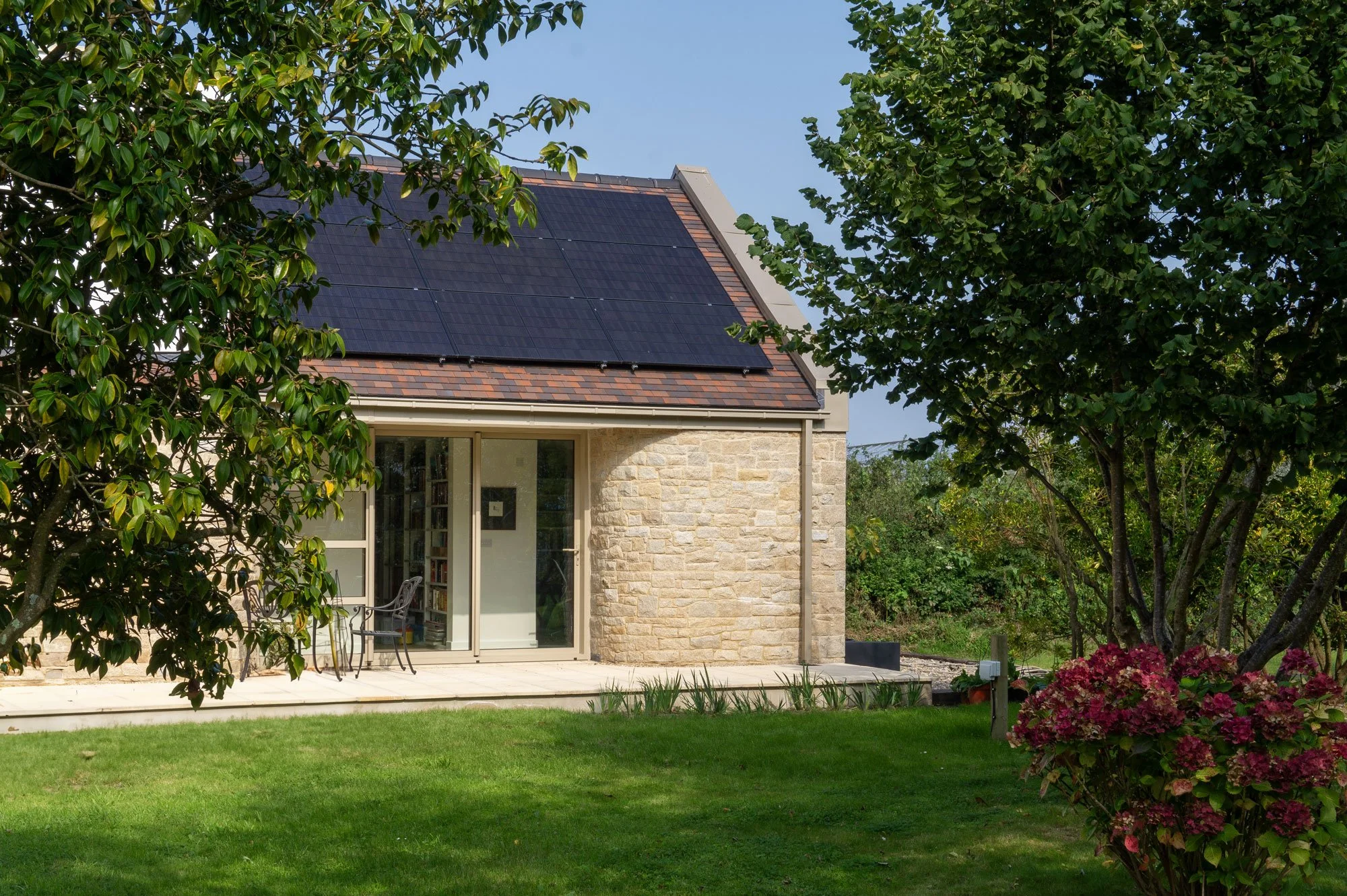 A cozy house with solar panels on the roof, surrounded by green trees and a well-maintained lawn.