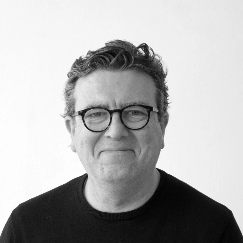 Patrick Walls - A man with glasses and a beard standing outdoors in front of leafy bushes.