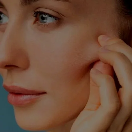 Nainen koskettaa kasvojansa ja katsoo sivulle.