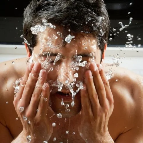 Nuori mies pesee kasvojaan vedellä käsillään.