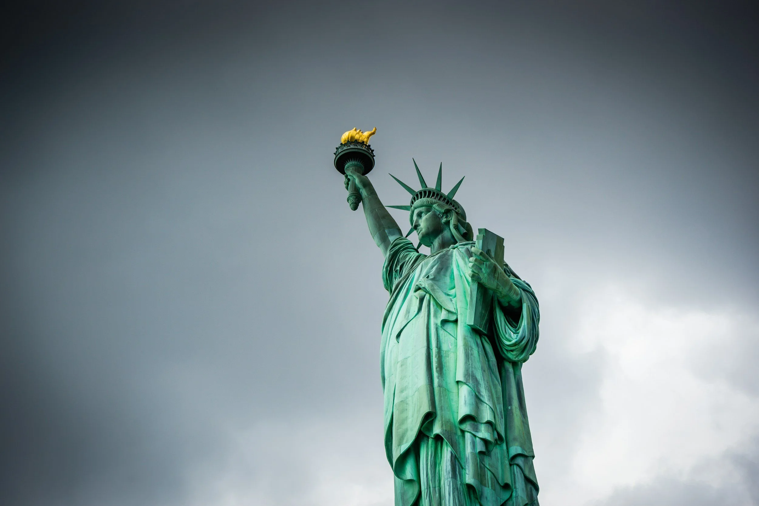 The Statue of Liberty standing on her pedestal with a dark, cloudy sky in the background.