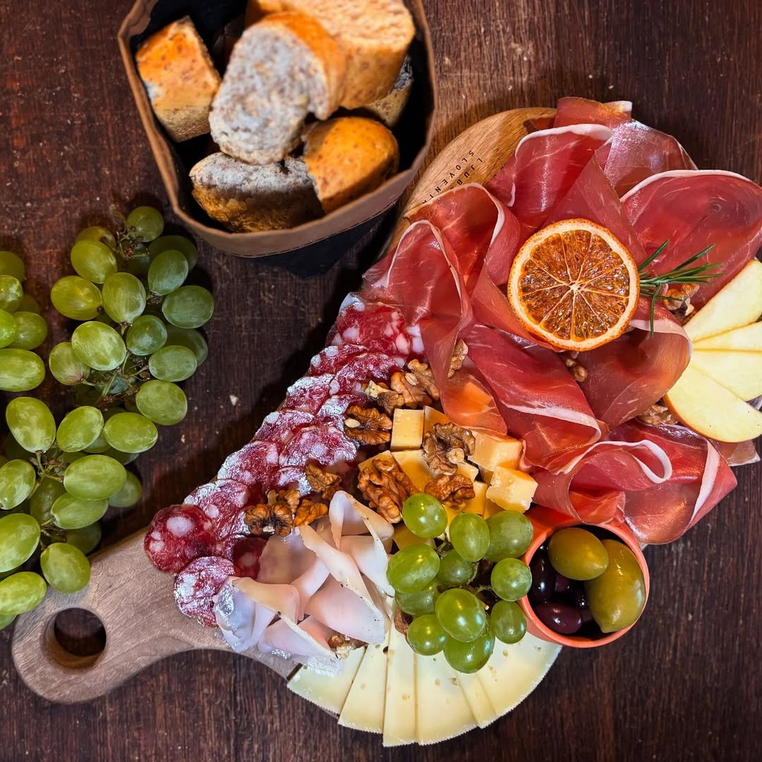 Charcuterie board with grapes, cheese, dried orange slice, prosciutto, walnuts, and bread on wooden table.