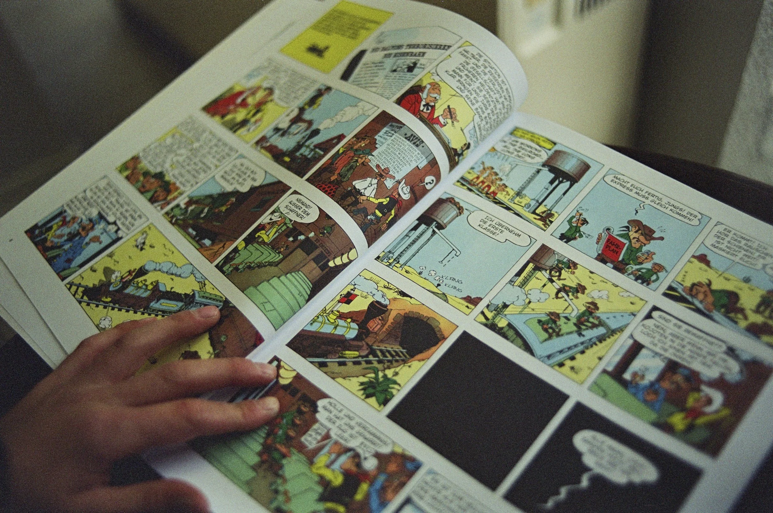 A person holding a comic book open, displaying colorful comic panels with characters and speech bubbles.