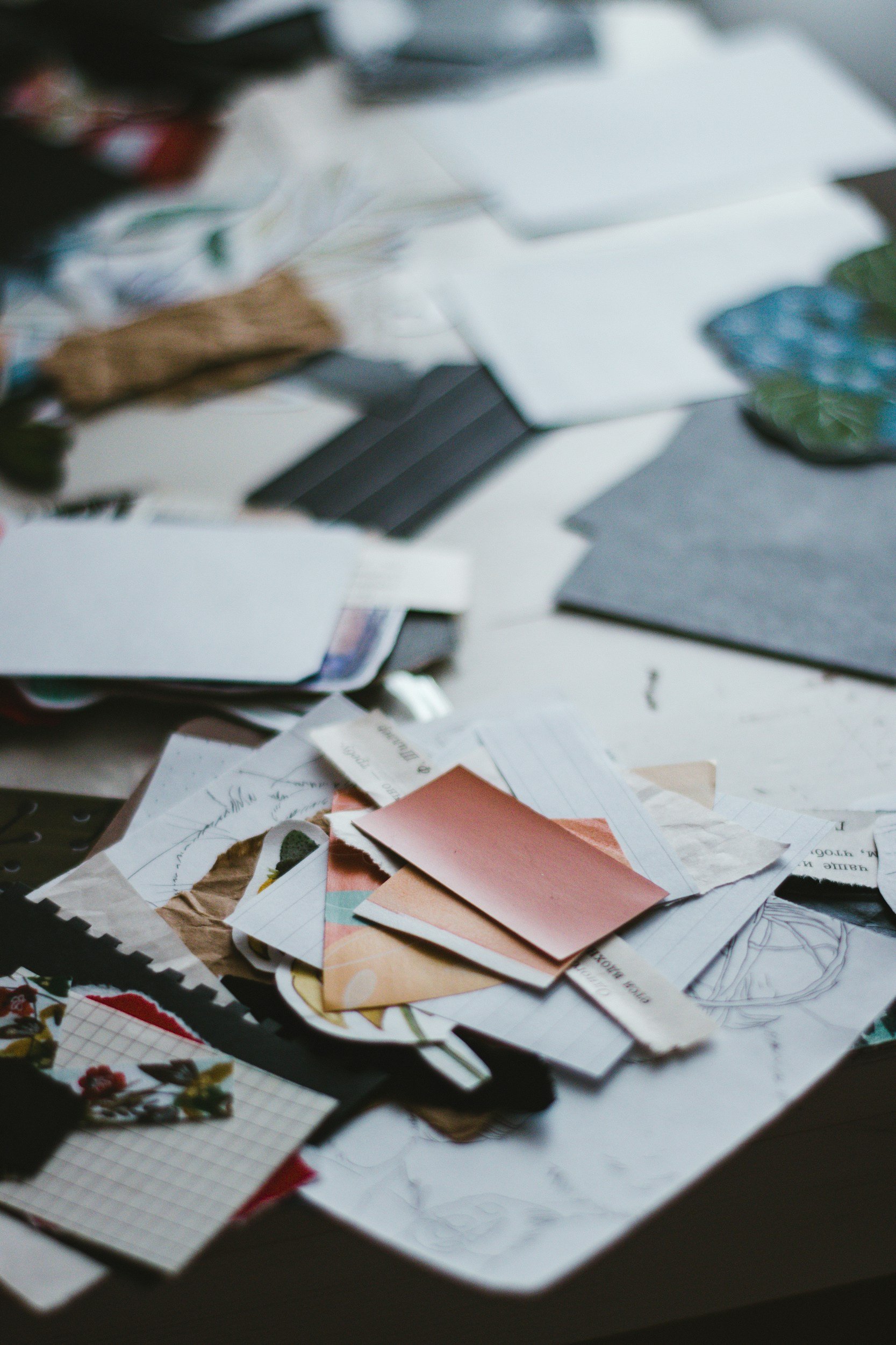 A cluttered desk with various papers, sketches, and fabric swatches scattered across the surface.