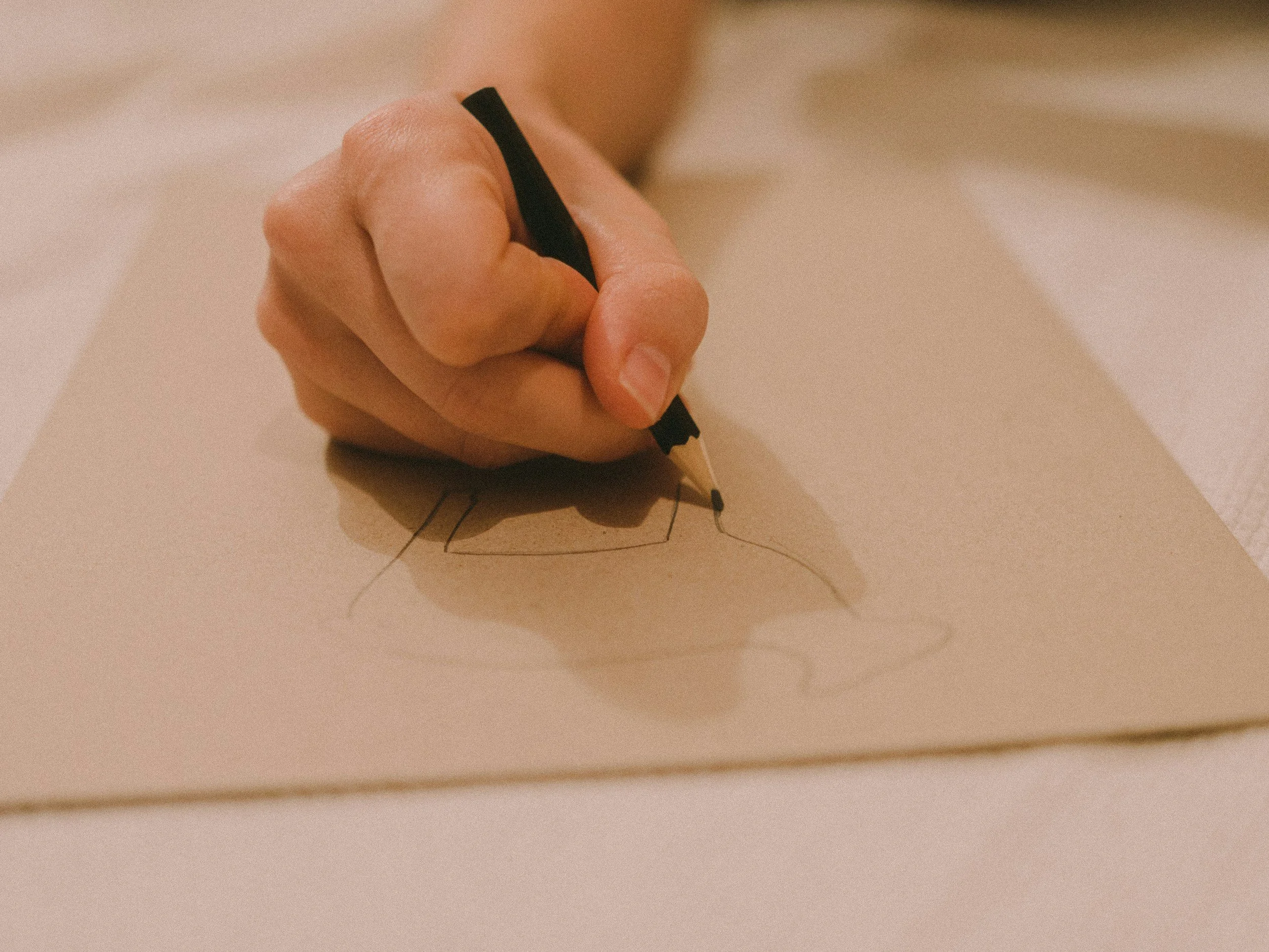A person drawing on a piece of paper with a black pen, creating a line art illustration.