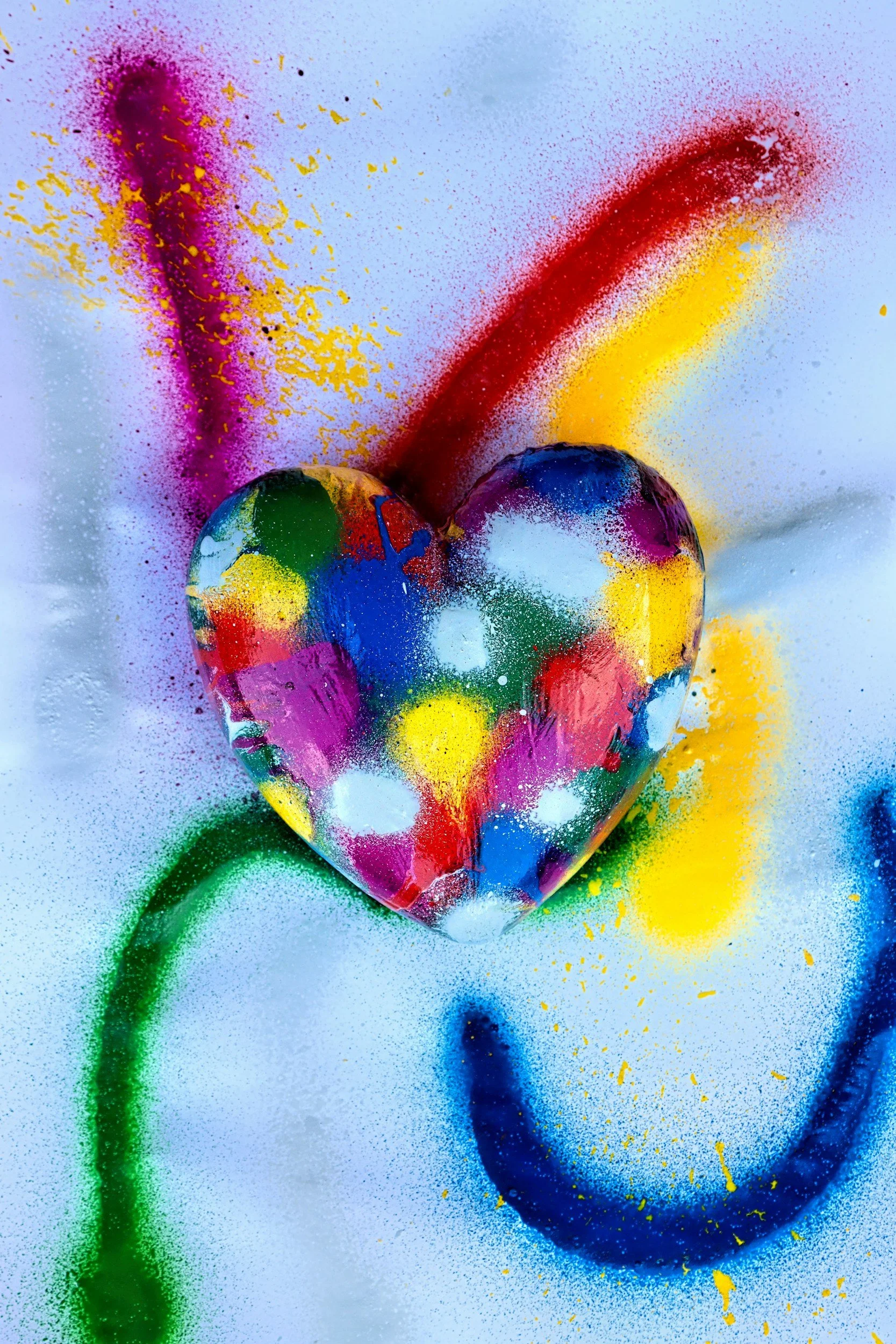Colorful spray paint art featuring a heart shape at the center, with various vibrant colors including pink, yellow, blue, green, white, and purple, against a light background with additional spray paint splashes.