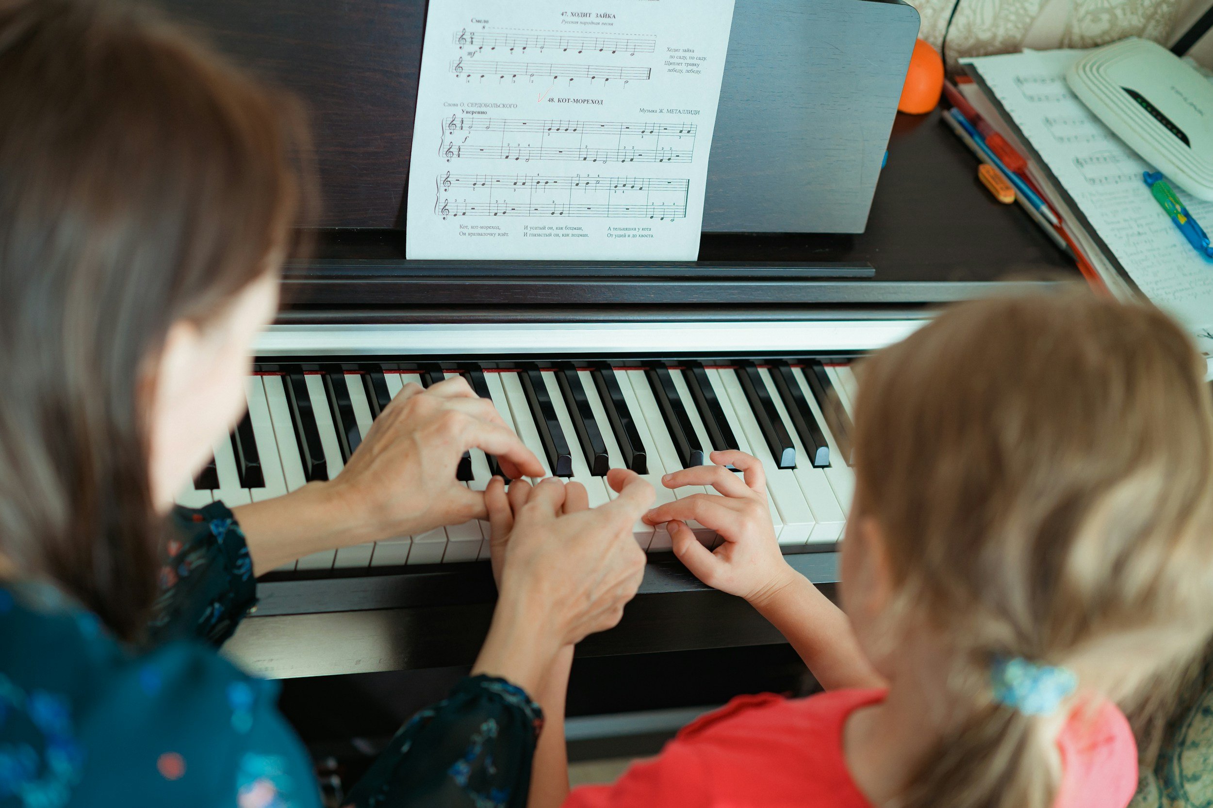 An adult and a young girl playing piano together, with sheet music on the music stand.