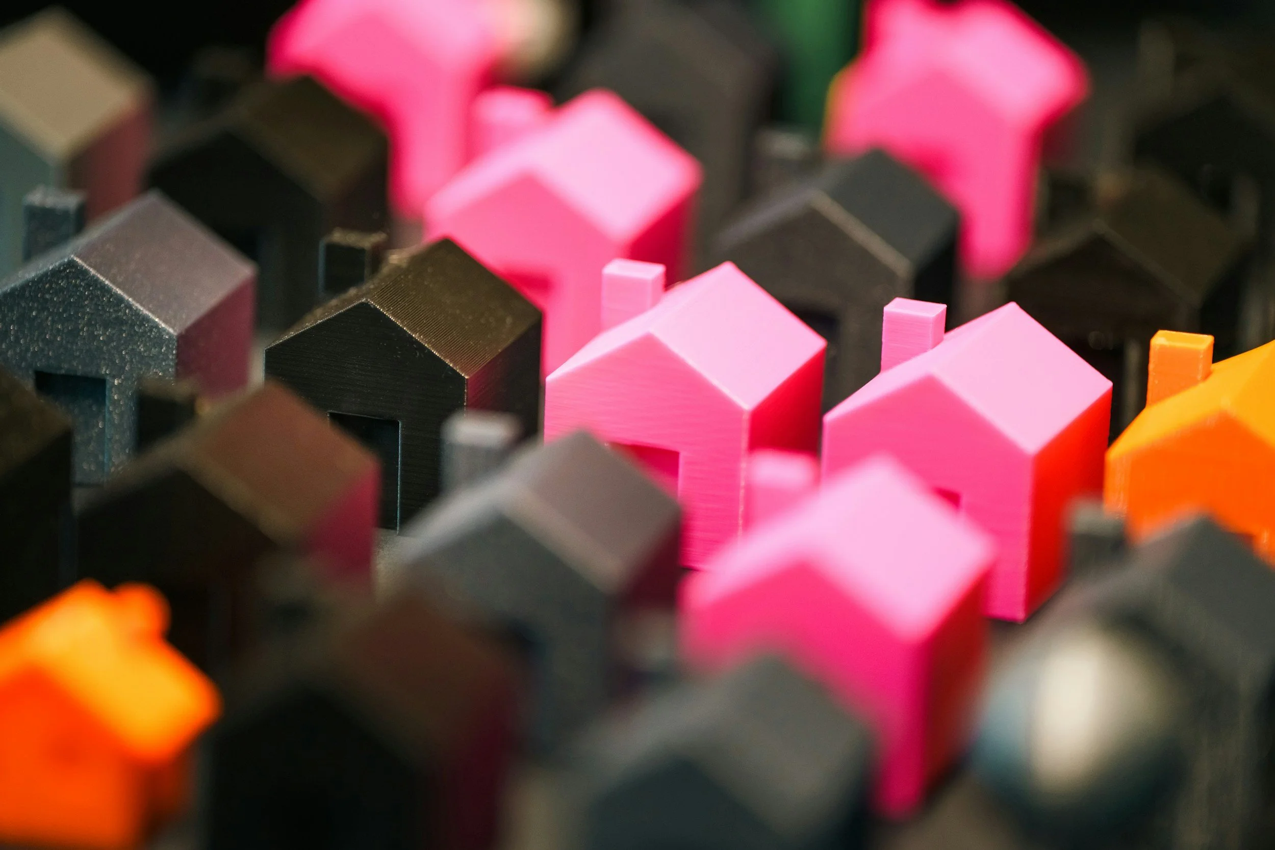 Close-up of colorful small house-shaped objects in pink, black, and orange, arranged closely together.