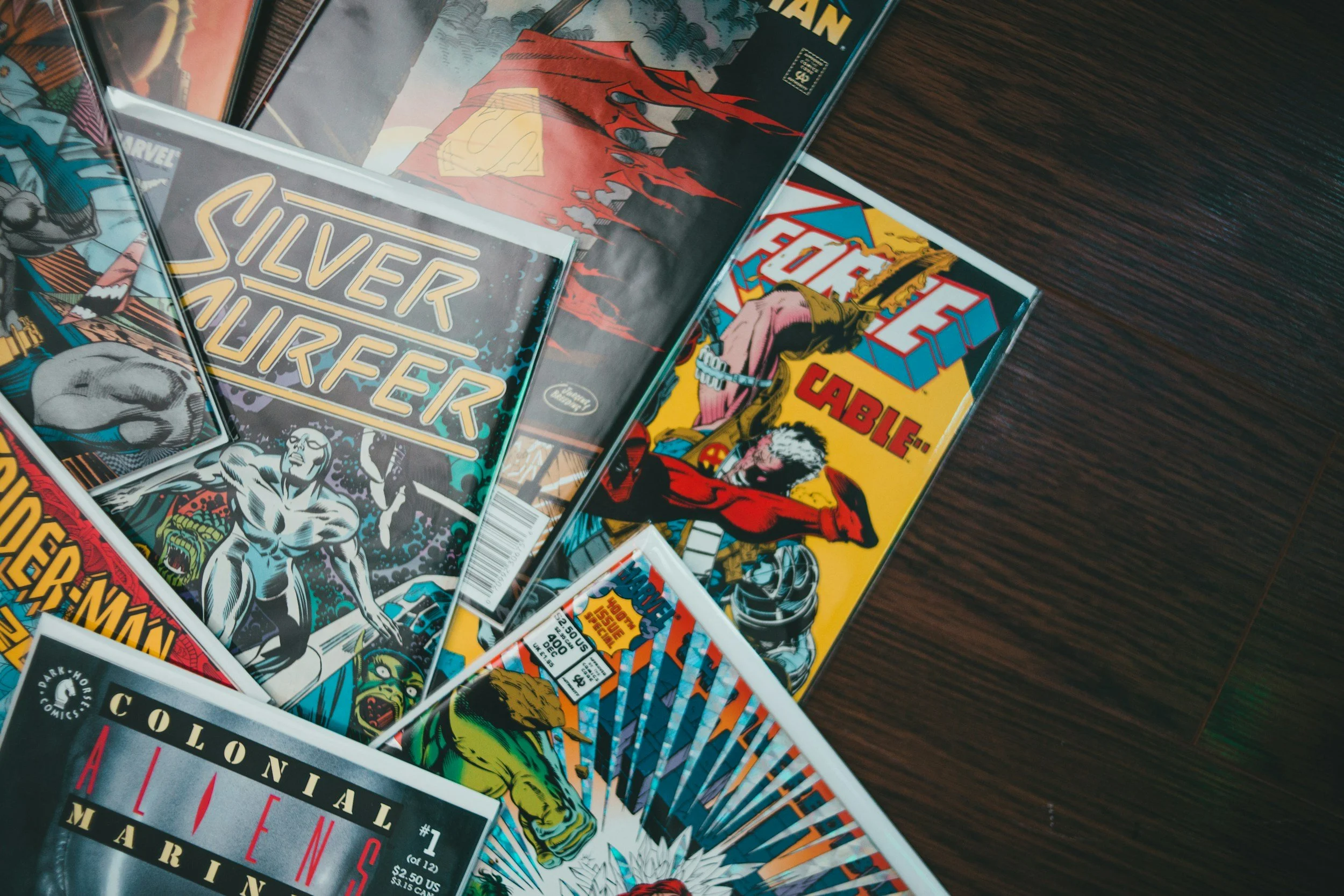 Collection of comic books on a wooden surface featuring titles like Silver Surfer, Thor, and other Marvel characters.