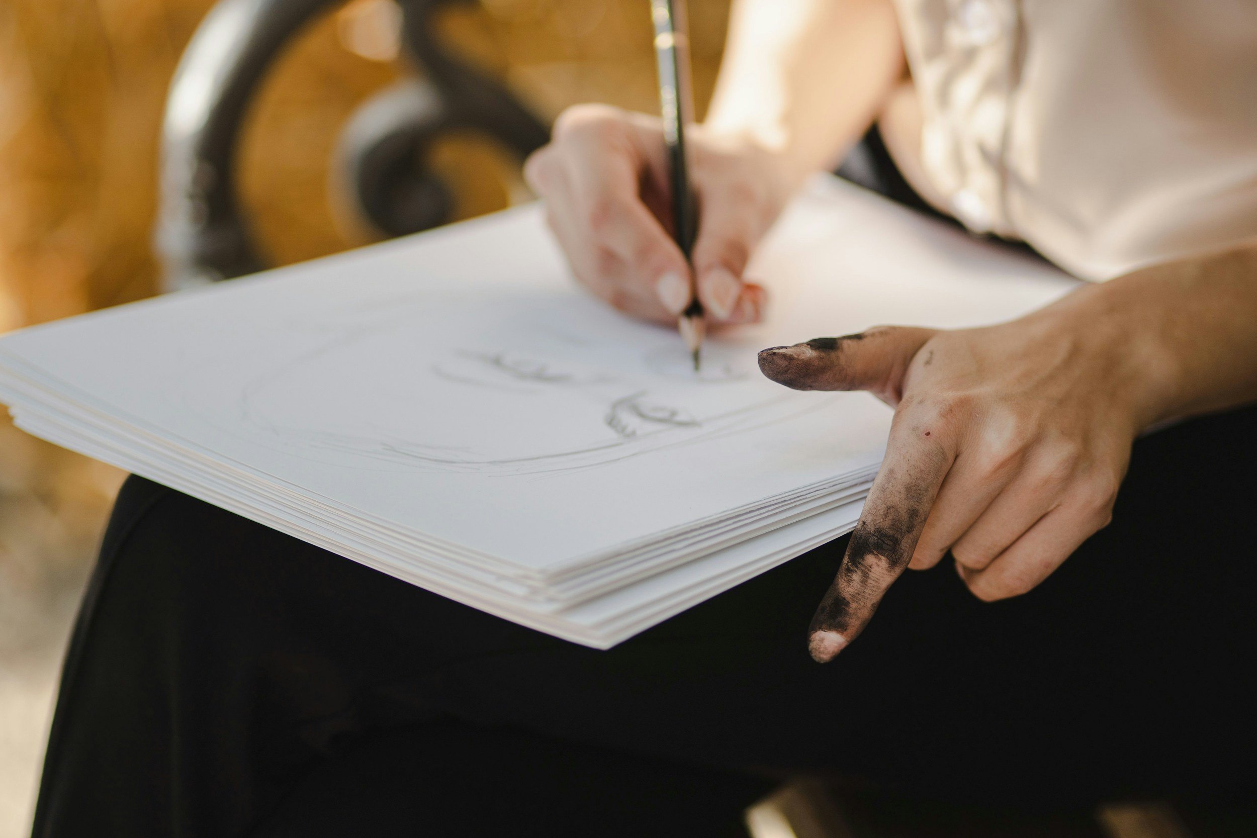 Person drawing on a piece of paper with a black pen, their fingers and hands are stained with ink or dirt.