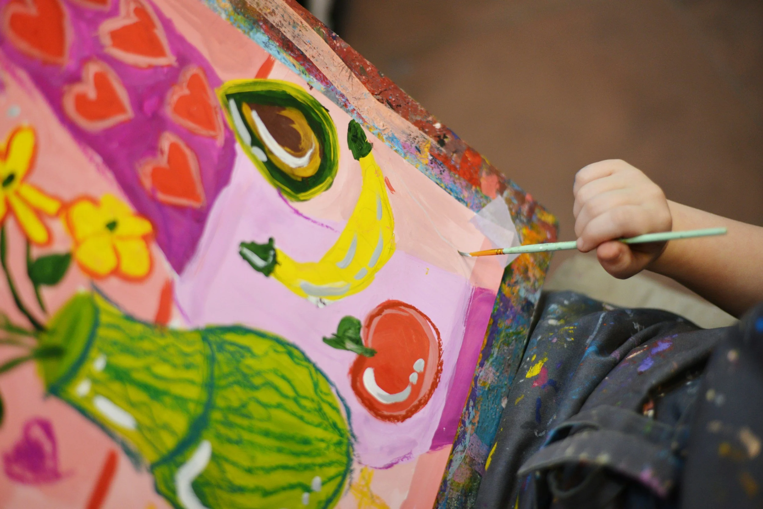 Close-up of a person painting a colorful, abstract floral and face design on a canvas with acrylic paints, using a small paintbrush.