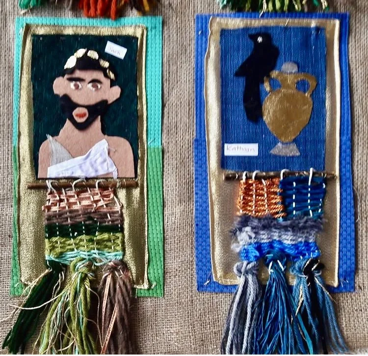 Two hand-crafted wall hangings with fabric and yarn, depicting ancient Greek figures. The left features a woman with dark hair, a gold headband, and a white toga, labeled 'Perik'. The right features a black bird and a gold vase, labeled 'Kithara'. Both hangings have woven yarn tassels at the bottom.