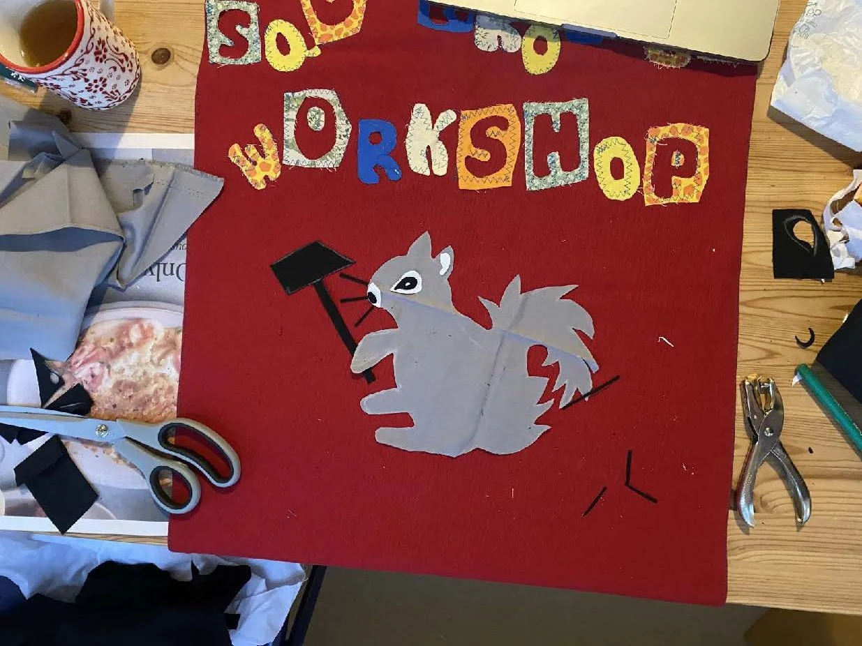 A craft project on a red mat reading 'Workshop' with colorful letter cutouts, a paper wolf holding a black gavel, scissors, and craft supplies surrounding it.