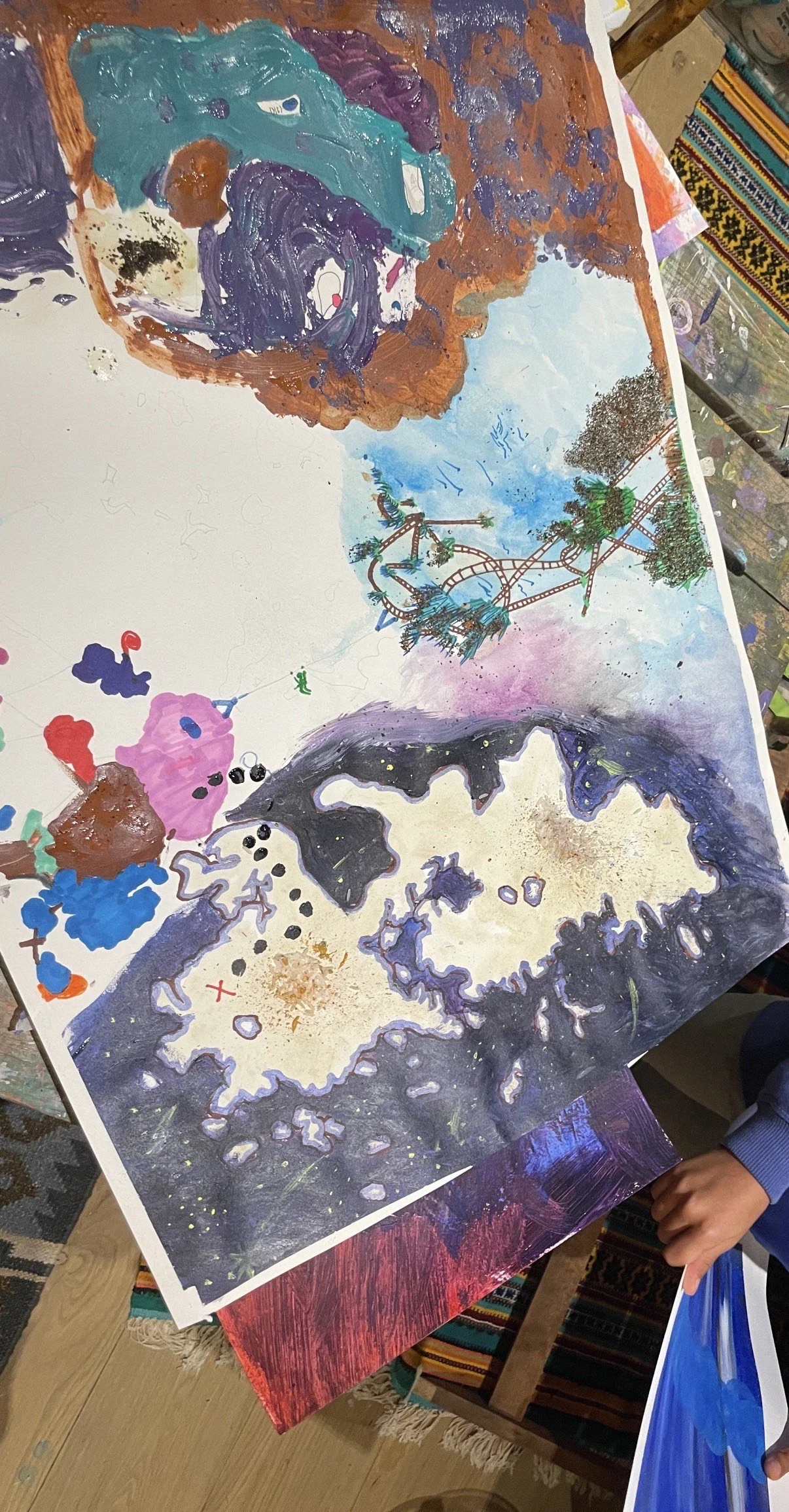 A colorful, abstract painting of a landscape with trees, a roller coaster, and a landmass, possibly representing a map.