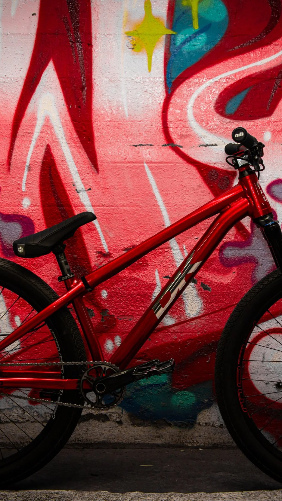 A red mountain bike leaning against a graffiti-covered wall with colorful abstract designs.