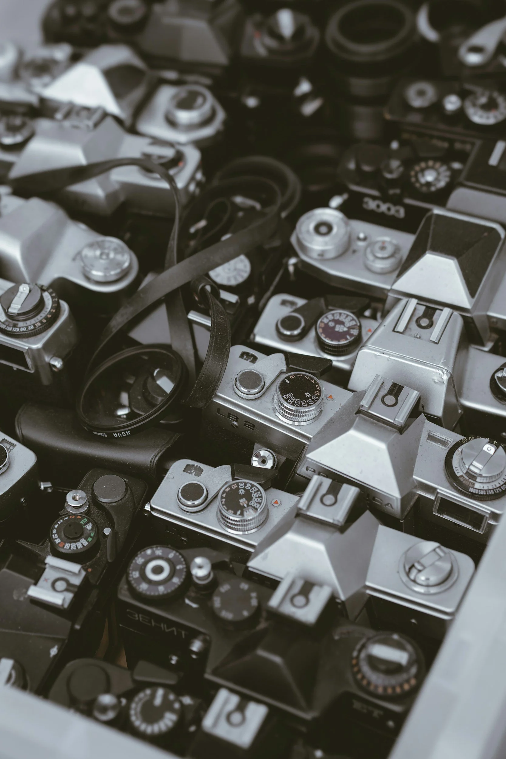 A collection of vintage cameras and camera parts piled together, showing various dials, lenses, and camera bodies.