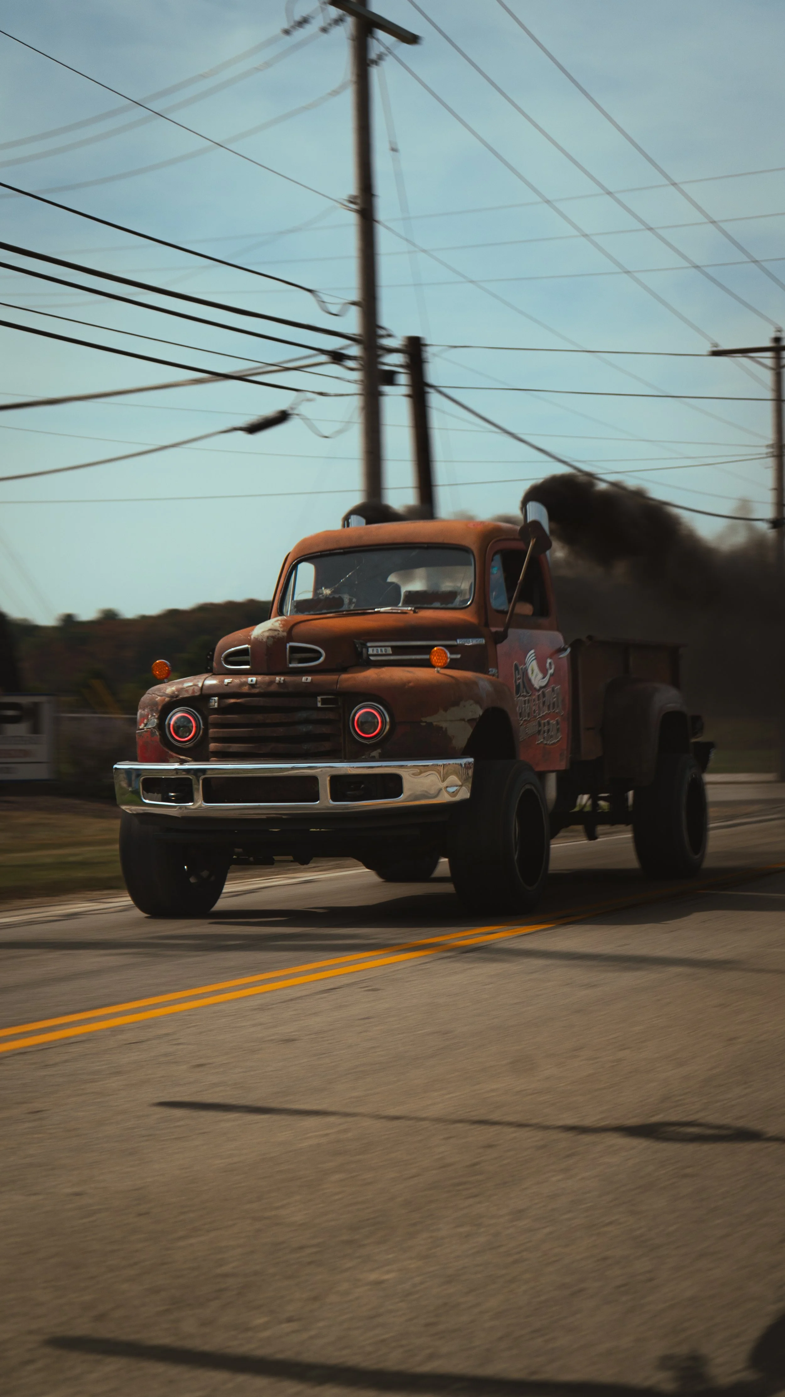 Old rusty pickup truck driving down the street with black smoke coming out of its exhaust pipe.
