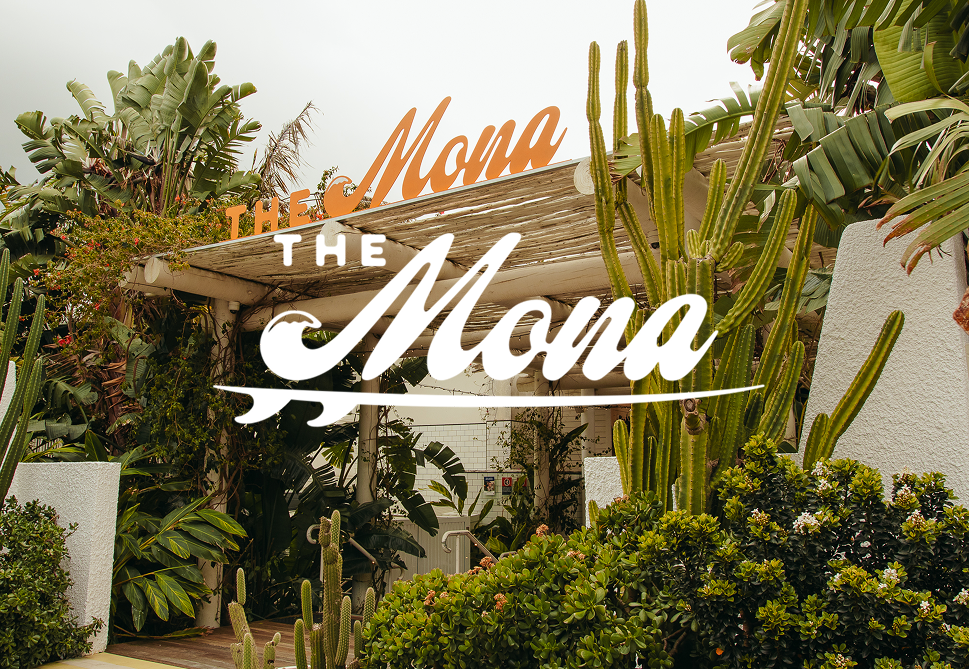 Outdoor scene with lush greenery and cacti surrounding a sign for "The Mona" restaurant