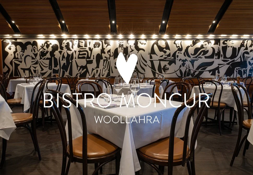 Elegant dining room with tables covered in white tablecloths, set with glasses and utensils, surrounded by dark wooden chairs, and a mural wall art in black and white in the background, with an overlay of a heart icon and text that reads 'Bistro Monc