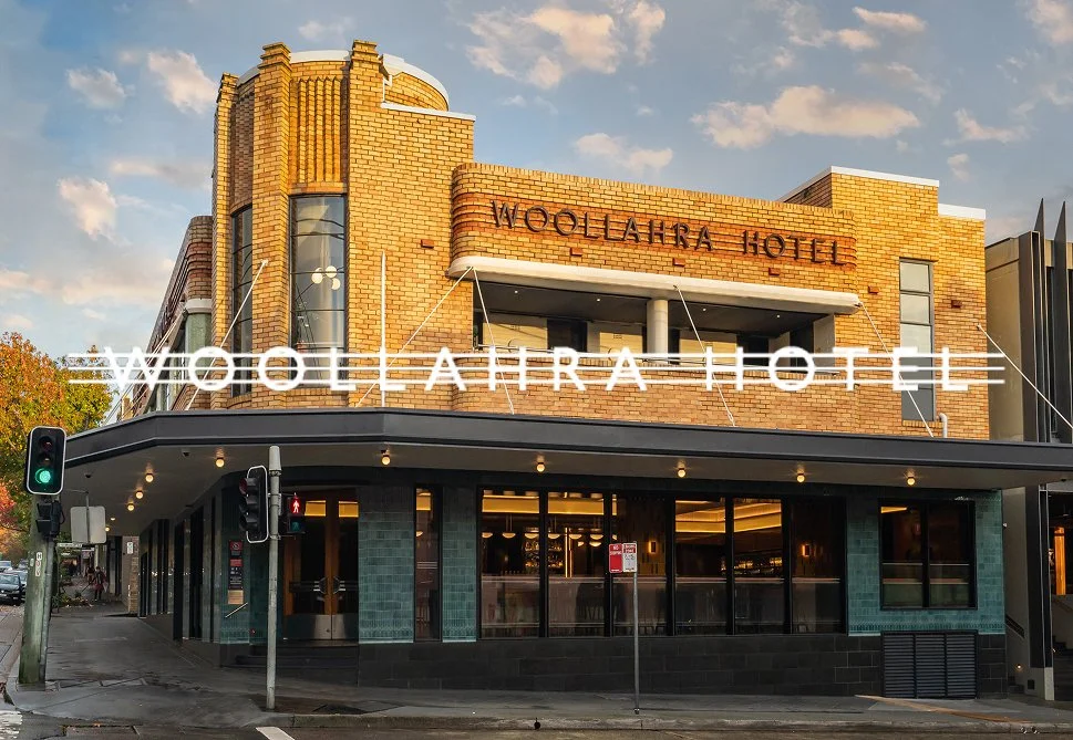 The Woollahra Hotel, a brick building with a large illuminated sign on the facade, located on a city street with traffic lights and pedestrian signals.