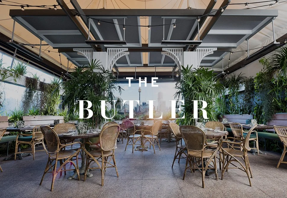 Indoor restaurant with wicker chairs, plants, and large windows with city view, titled 'The Butler' in white text.