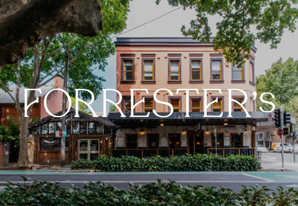A three-story building with large windows on a tree-lined street, featuring a dark awning and outdoor seating area at street level, with the text 'Forrester's' overlaying the image.