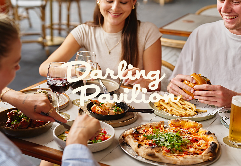 People enjoying a meal at a restaurant with pizza, fries, salad, wine, and beer, smiling and conversing.