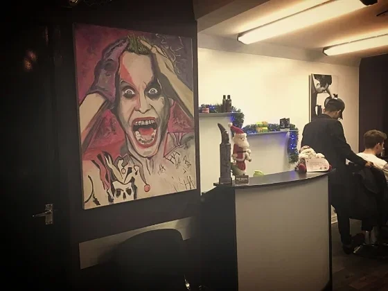 A colorful painting of a woman with a manic expression, holding her head with both hands, displayed on a wall in a room decorated for the holidays with Christmas ornaments and a small Santa figurine.