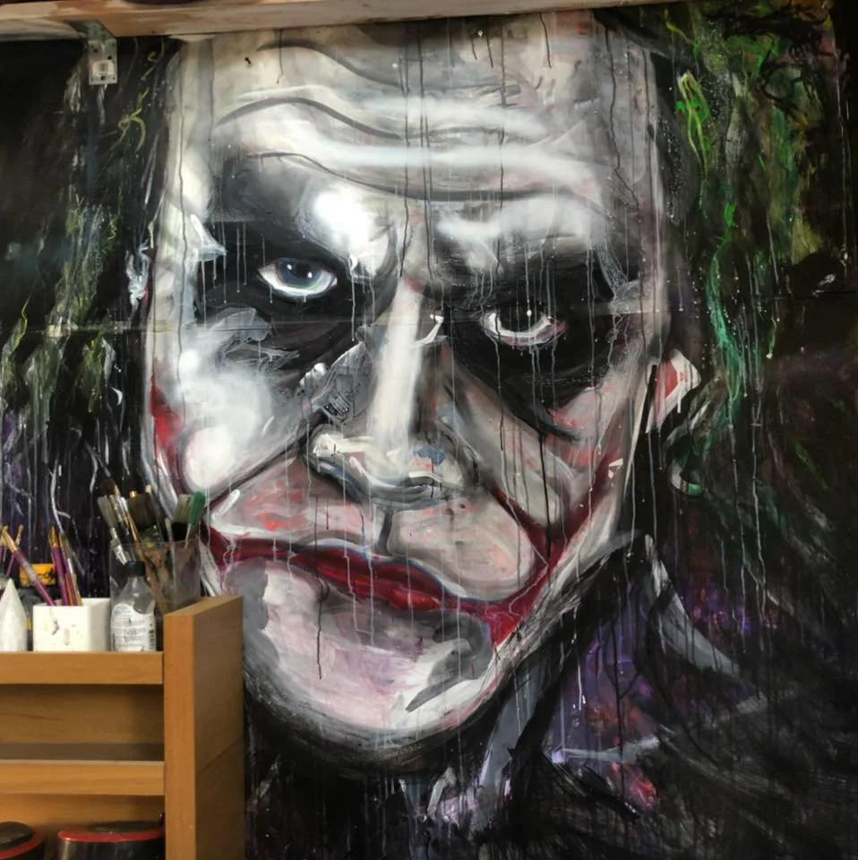 Colorful graffiti-style mural of the Joker with a sad expression, painted with splashes and drips of paint.