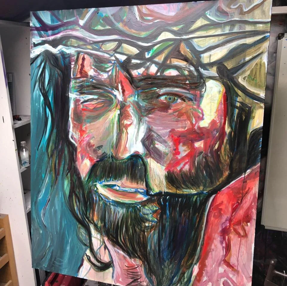 Abstract colorful painting of a man's face with long hair, a beard, and one eye closed. The artwork features expressive brushstrokes and vibrant hues.