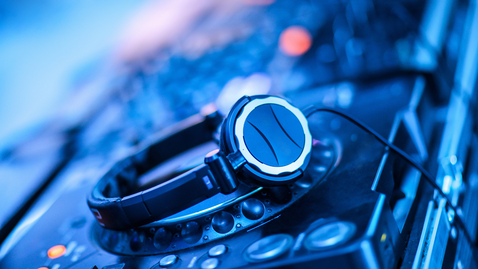 Cuffie da DJ nere posate su un mixer audio con luci blu e dettagli metallici.