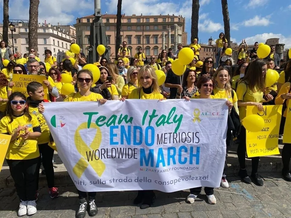 Gruppo di persone con magliette gialle e palloncini gialli che partecipano a una marcia per la consapevolezza della Encefalomielite Miosite. Slogan e banner sulla coscienza e sensibilizzazione sulla condizione.