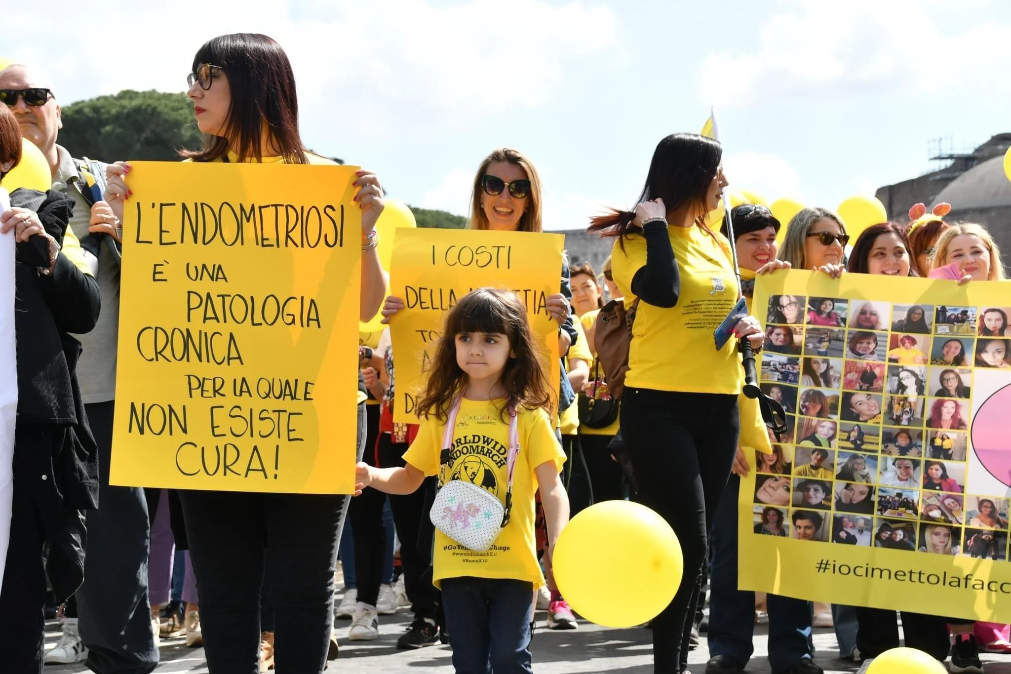 Gruppo di persone in procinto di partecipare a una manifestazione o una marcia, molte indossano magliette e portano palloncini gialli, con alcuni che tengono cartelli con messaggi riguardanti la salute femminile e la prevenzione del cancro al endomet