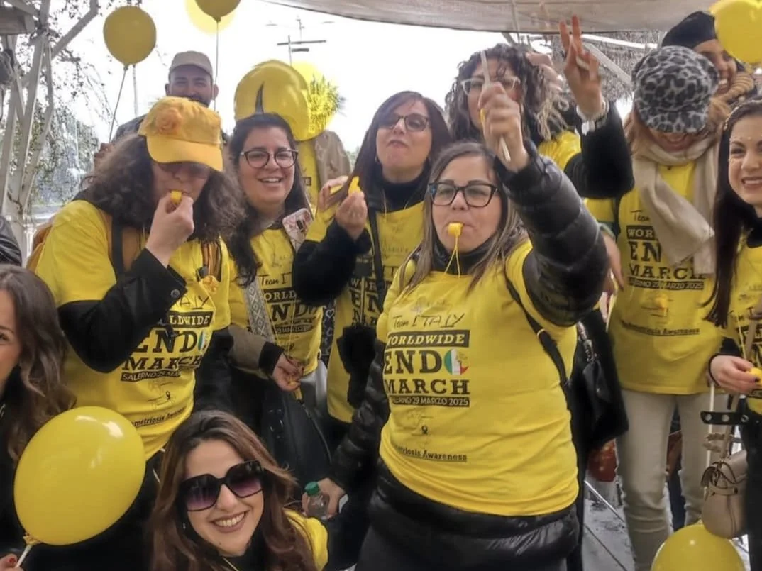 Gruppo di persone che partecipano a un evento di beneficenza, indossando magliette gialle e cappelli, con palloncini gialli, che celebrano la marcia mondiale per la consapevolezza del morbo di Alzheimer.