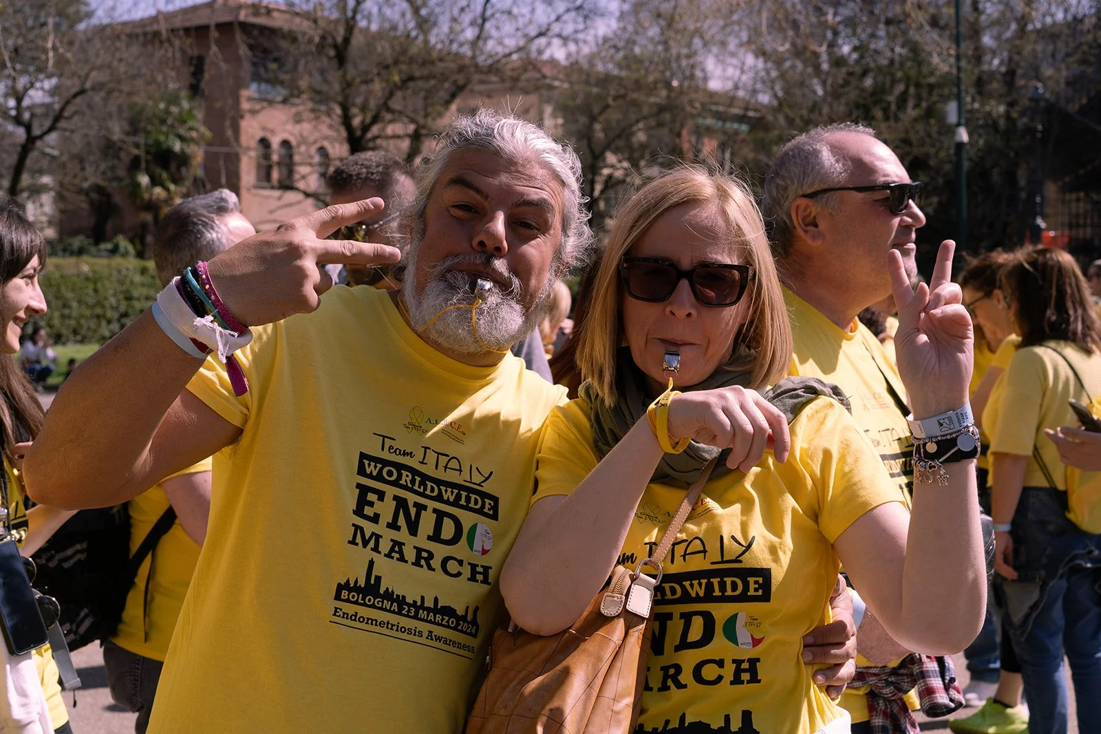 Gruppo di persone vestite con magliette gialle che partecipano alla Marcia mondiale per la fine della endometriosi a Bologna, Italia, il 23 marzo 2024. Le persone fanno peace sign e sorridono alla fotocamera in un parco.