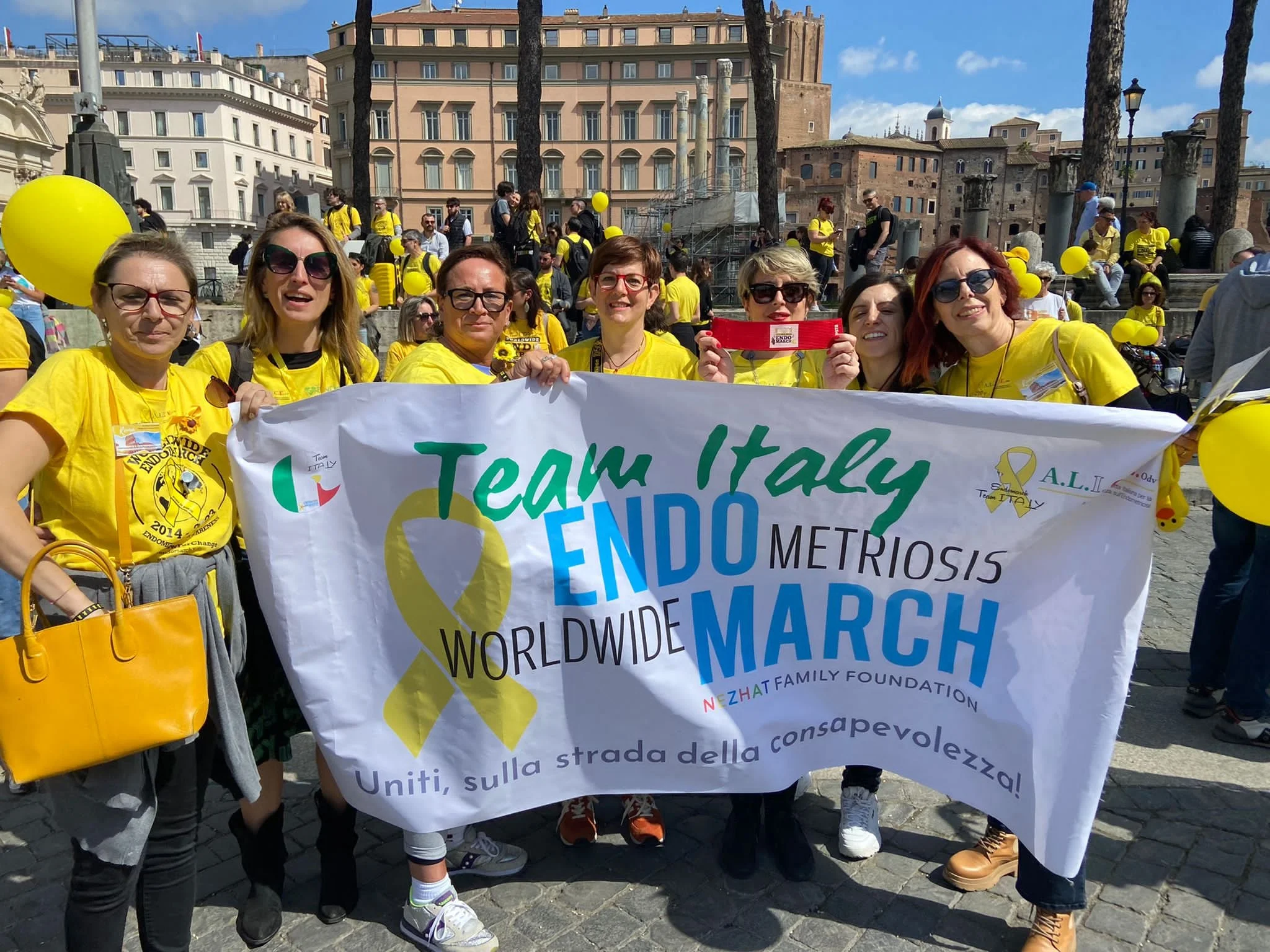Gruppo di persone che partecipano alla marcia mondiale contro la metropatia, con magliette gialle e cartelloni, in un'area urbana.