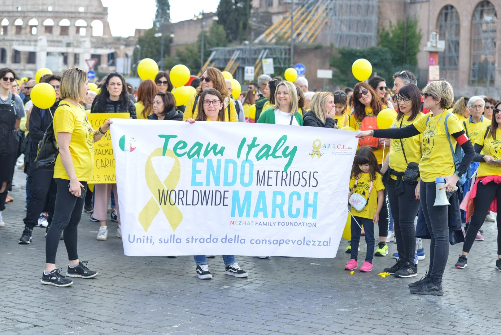 Gruppo di persone durante una marcia con palloncini gialli, che tengono uno striscione per la sensibilizzazione sulla endometriosi, con messaggi di unità e consapevolezza.