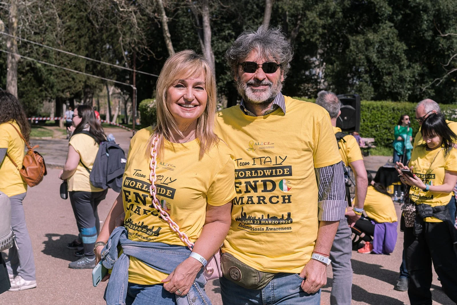 Due persone, una donna e un uomo, sorridenti, si abbracciano durante una manifestazione di sensibilizzazione sull'endometriosi, indossando magliette gialle con scritte in inglese e italiano.