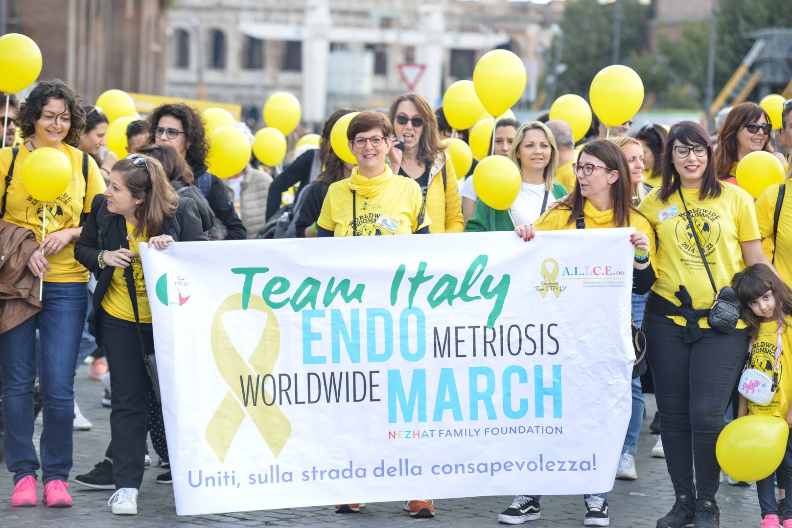 Gruppo di persone che partecipano a una marcia di sensibilizzazione contro la metrombioside endo, portando un grande striscione con scritto 'Team Italy Endo Metriosis Worldwide March' e palloncini gialli.