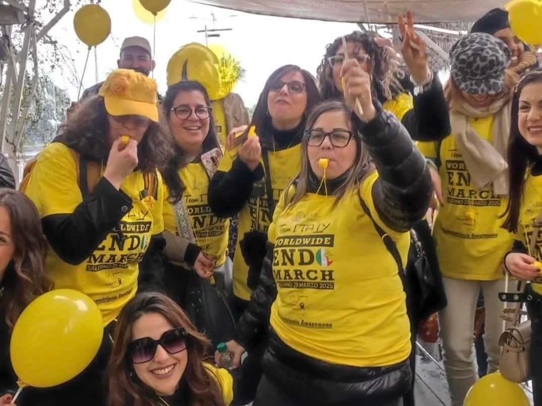 Gruppo di persone che partecipano a un evento di sensibilizzazione e solidarietà, indossando magliette gialle con entusiasmo, decorazioni di palloncini gialli e bandiere, in un ambiente esterno.