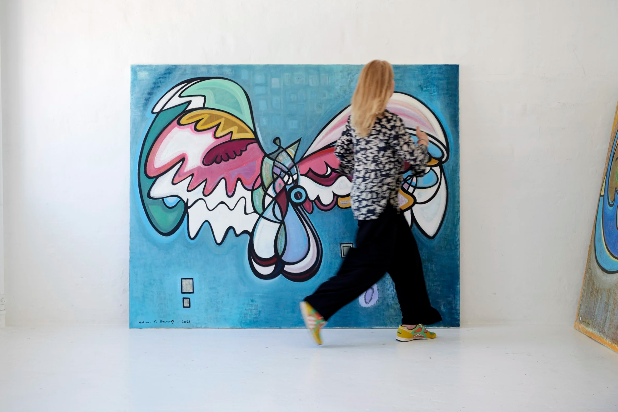 A person walking in front of a colorful abstract painting in an art gallery.