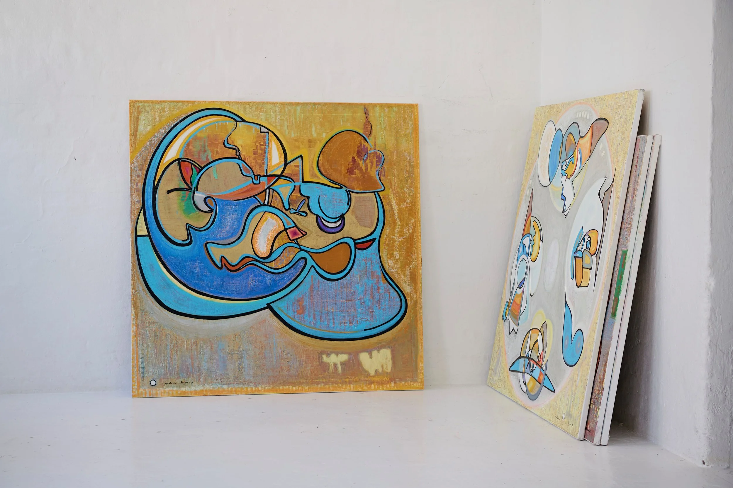 Abstract colorful paintings with swirling shapes and lines, leaning against a plain white wall.